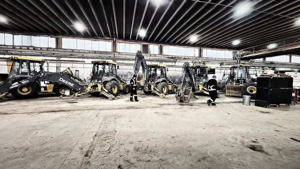 Six John Deere backhoes and loaders lined up in the Mach 6 shop bay with technicians working