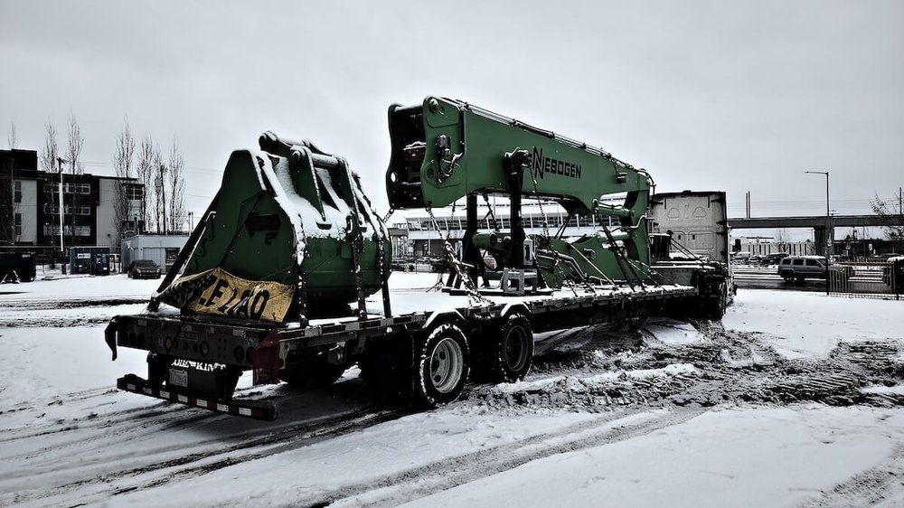 Sennebogen material handler on a lowboy trailer, the machine Mach 6 services